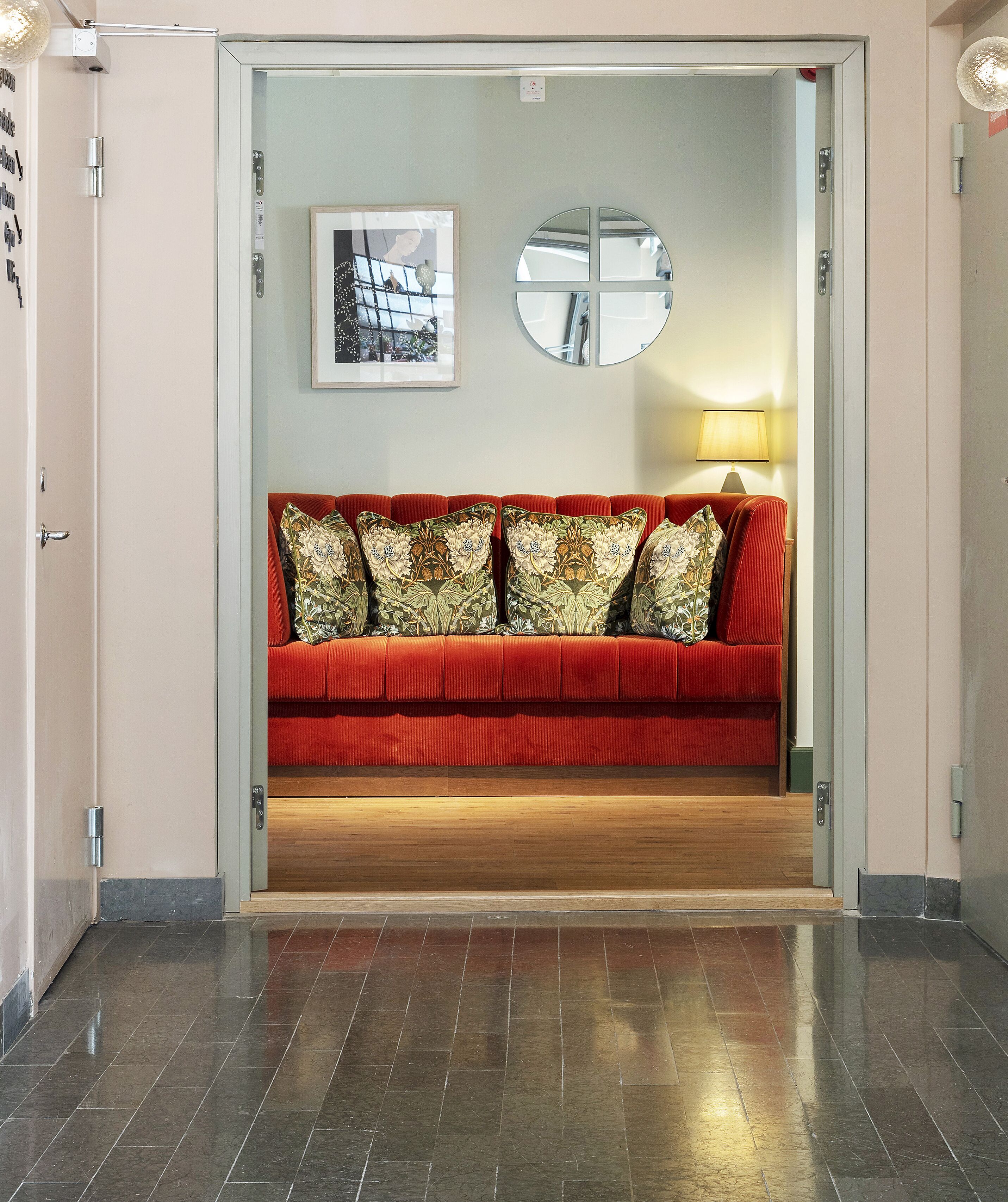 Un sofá rojo con cojines estampados en un pasillo con suelo de madera y una puerta que da a otra habitación.