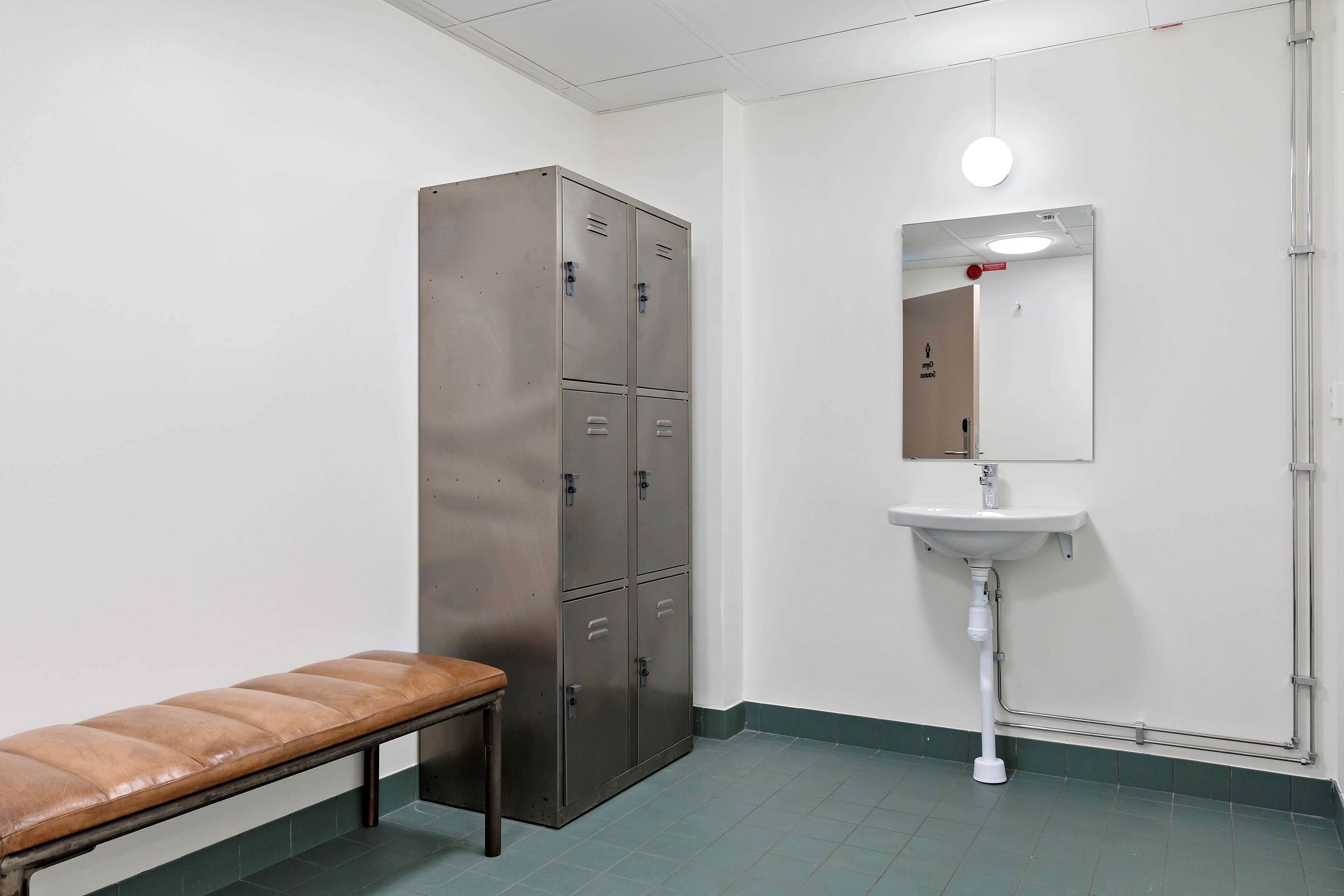 A restroom with a bench, a metal locker, and a sink with a mirror.
