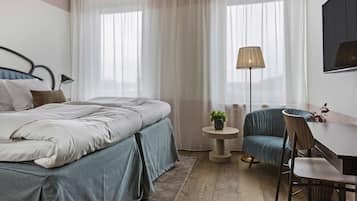 Una camera d'albergo moderna con un letto, un tavolino rotondo, una sedia, una lampada e una pianta.