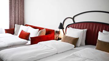 Habitación de hotel con cama doble, cabecera tapizada de rojo y mesita de noche con lámpara.