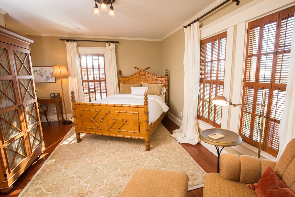 A bedroom with a wooden bed, a small round table, a sofa, and a large window with wooden shutters.