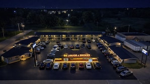 Un estacionamiento con varios coches, un edificio con la leyenda '66 Liquor & Smokes' y un cartel que dice 'ABIERTO'.