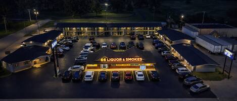 Un estacionamiento con varios coches, un edificio con la leyenda '66 Liquor & Smokes' y un cartel que dice 'ABIERTO'.