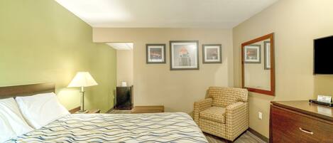 Une chambre d’hôtel avec un lit, une chaise, une commode et des tableaux encadrés accrochés au mur.