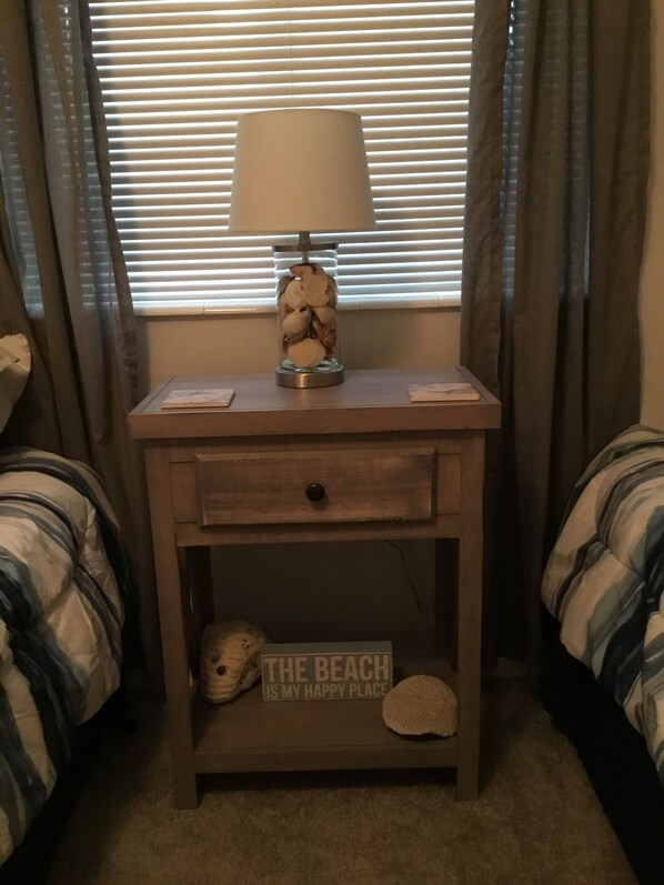 A bedroom with a nightstand, a lamp, a decorative item, and a sign on the nightstand.
