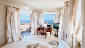 Een slaapkamer met een bed, een bureau en een televisie. Vanuit de kamer is er uitzicht op zee.