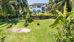 A two-story house with a stone wall and a well-maintained garden with palm trees and shrubs. - Casablanca Curral Beach (ilhabela)