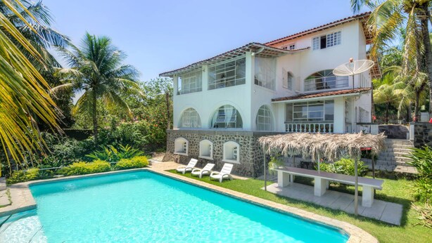 A two-story house with a swimming pool, surrounded by lush greenery and palm trees. - Casablanca Curral Beach (ilhabela)