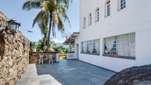 A white building with large windows and a stone wall. - Casablanca Curral Beach (ilhabela)