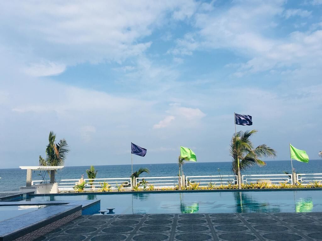 A pool area with a view of the ocean, palm trees, and flags.