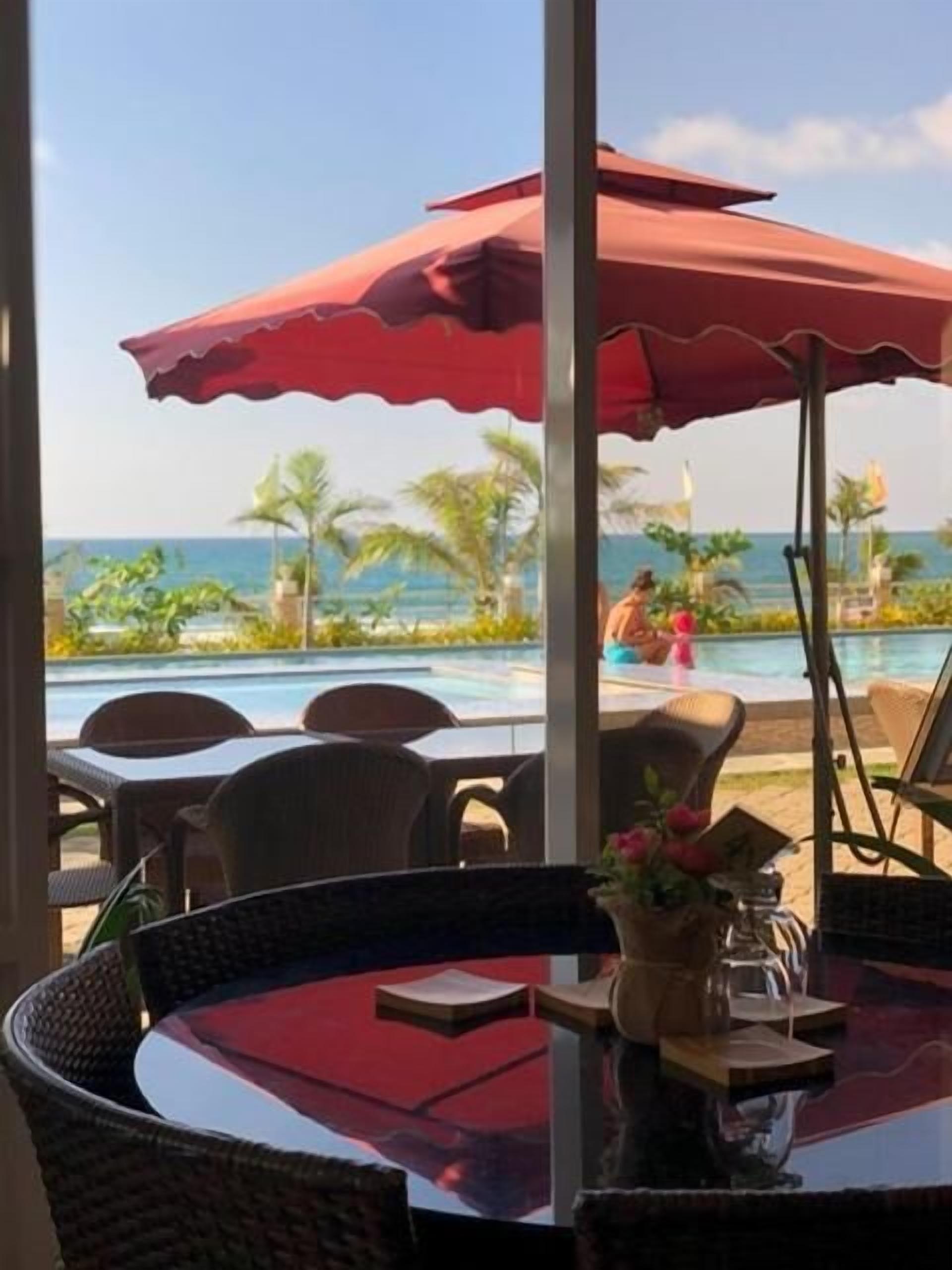 A dining area with a view of the ocean, outdoor seating, and a pool.