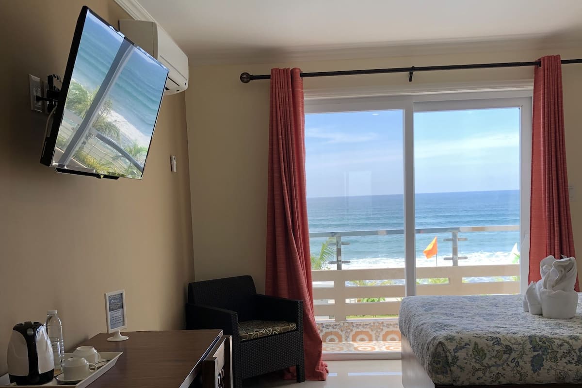 Ein Hotelzimmer mit Bett, Schreibtisch, Fernseher und einem Balkon mit Meerblick.