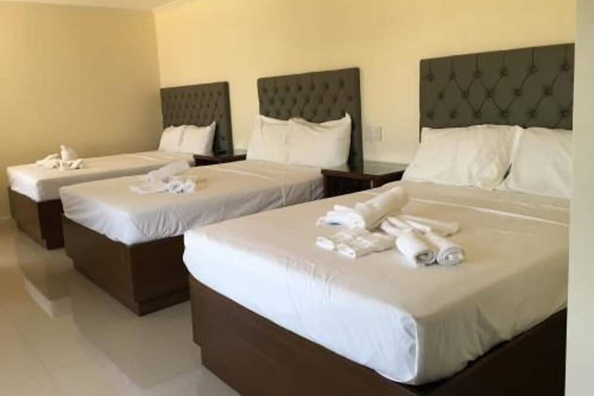 Ein Hotelzimmer mit drei Einzelbetten, jeweils mit Kopfteil und weißer Bettwäsche.