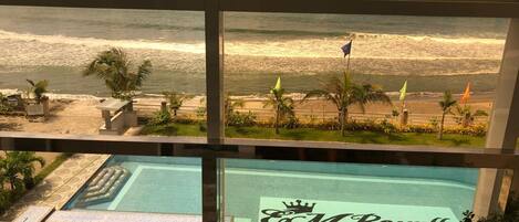 A view of a beach with palm trees and flags, and a pool area with a sign reading "M Royale".