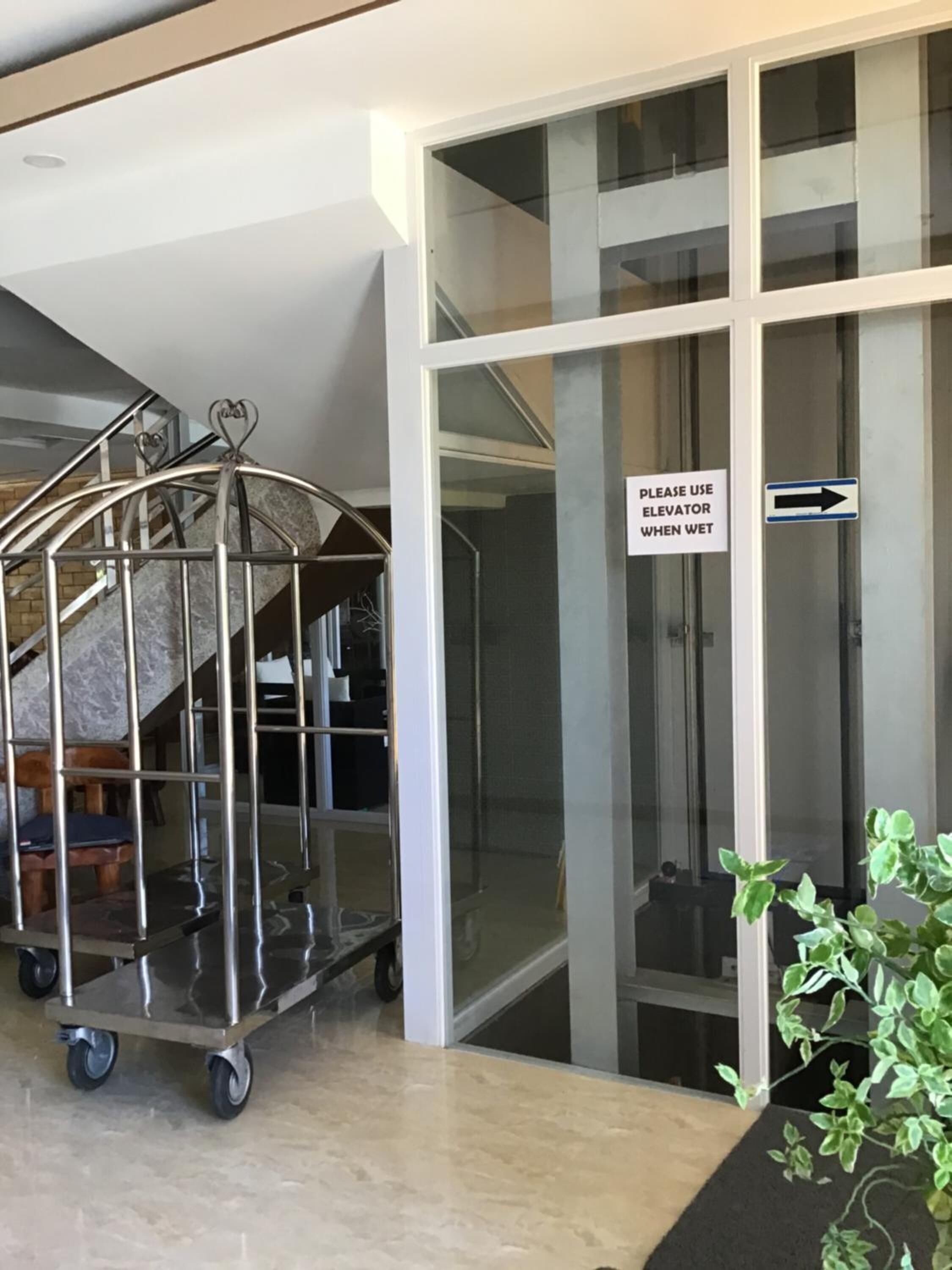 A modern interior with a glass elevator door, a metal cart, and a sign advising to use the elevator when wet.