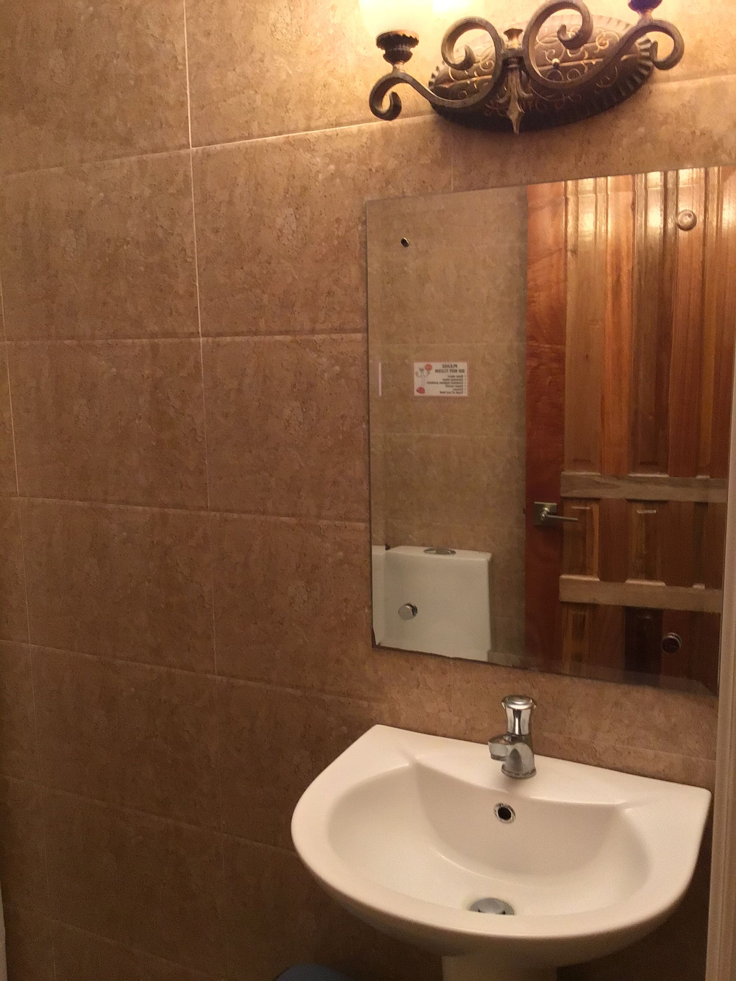 Une salle de bain avec un lavabo blanc, un miroir et une porte en bois.