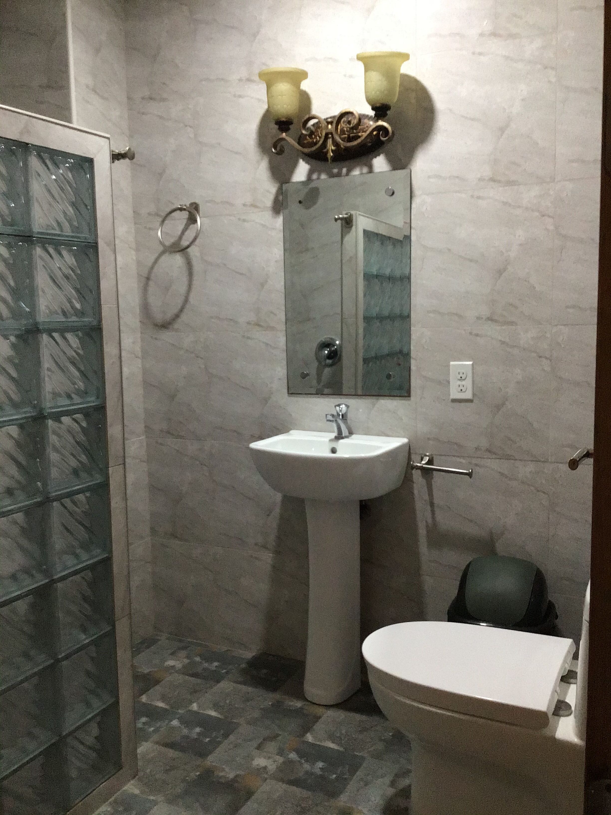 A bathroom with a glass shower enclosure, a pedestal sink, and a toilet.
