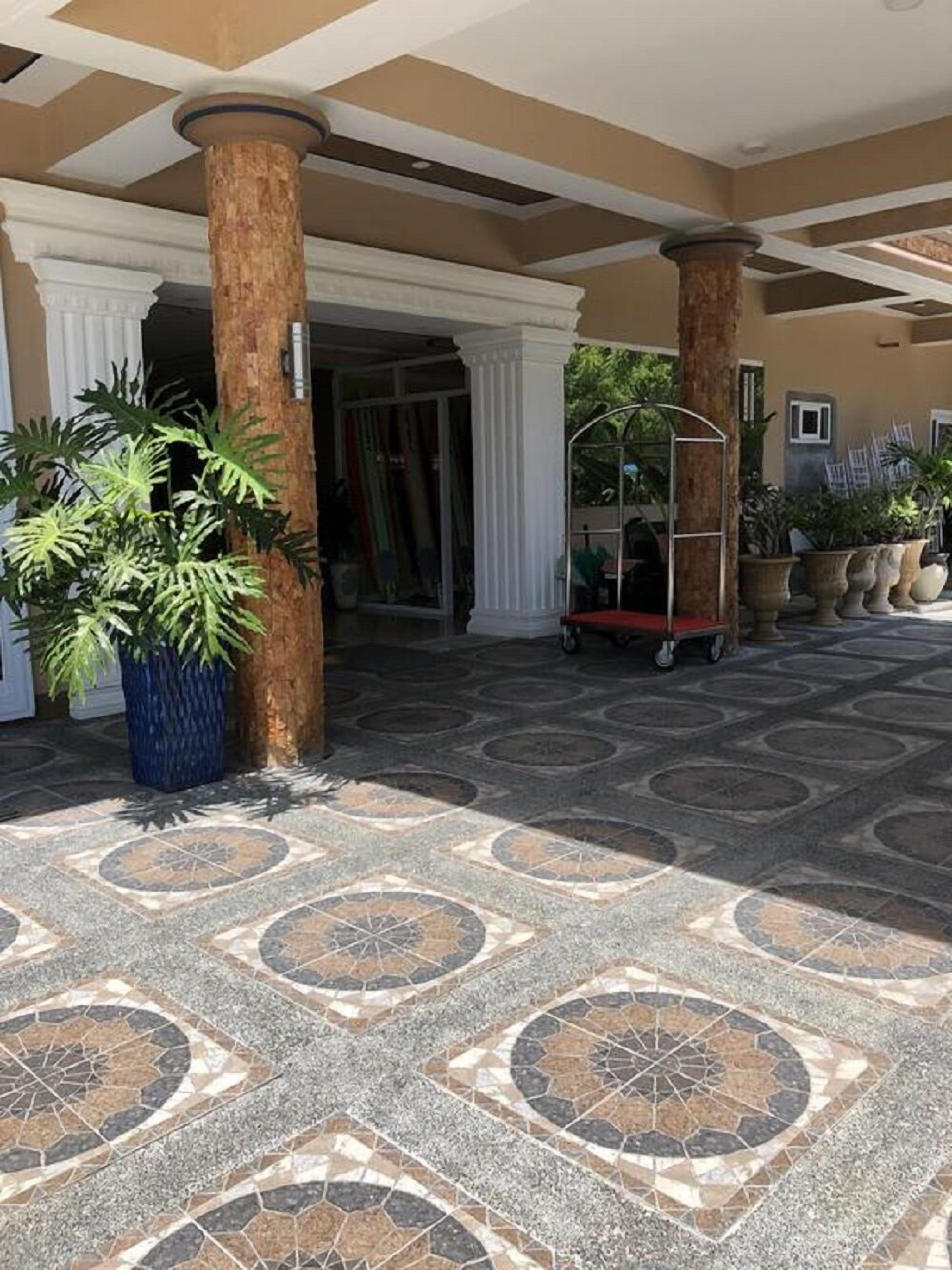 A covered outdoor area with patterned tile flooring, columns, and potted plants.