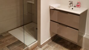 Un bagno moderno con box doccia in vetro, lavabo bianco con specchio e pavimento piastrellato.