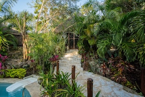 A stone staircase surrounded by lush tropical plants leading to a thatched-roof structure. - Aldea JOYAH (Tulum)
