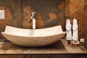A curved white ceramic sink with a modern faucet, two white towels, and two small bottles of soap on a wooden countertop. - Aldea JOYAH (Tulum)
