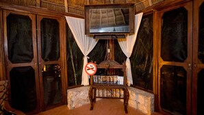 A room with a television mounted on the wall, wooden doors, and a stone bench. - Aldea JOYAH (Tulum)