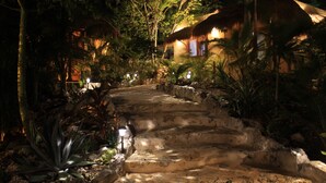 A thatched-roof building surrounded by lush vegetation and stone steps leading to it. - Aldea JOYAH (Tulum)