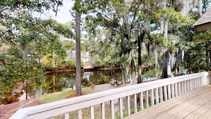 A wooden deck with a white railing overlooking a body of water, surrounded by trees with Spanish moss. - Very Nice Home Located on the 11-Mile Lagoon with Its Own Large Private Pool! (Hilton Head)