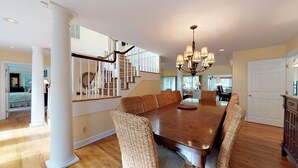 A spacious dining area with a large wooden table, wicker chairs, and a chandelier. - Very Nice Home Located on the 11-Mile Lagoon with Its Own Large Private Pool! (Hilton Head)