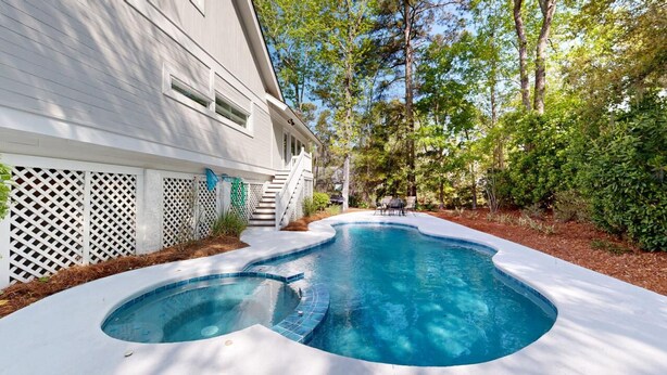 A swimming pool with a curved edge, surrounded by a white fence and lush greenery. - Very Nice Home Located on the 11-Mile Lagoon with Its Own Large Private Pool! (Hilton Head)