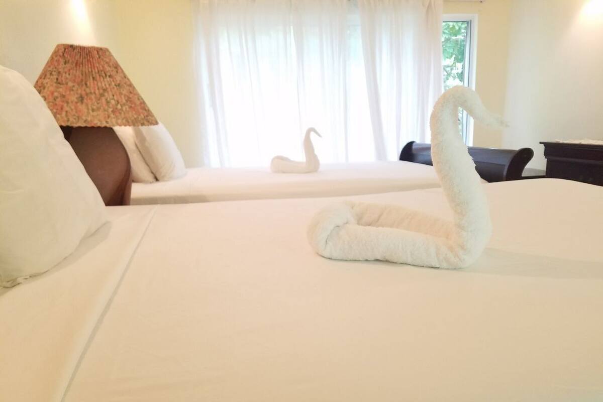 A hotel room with two beds, a lamp, and a swan-shaped towel on the bed.