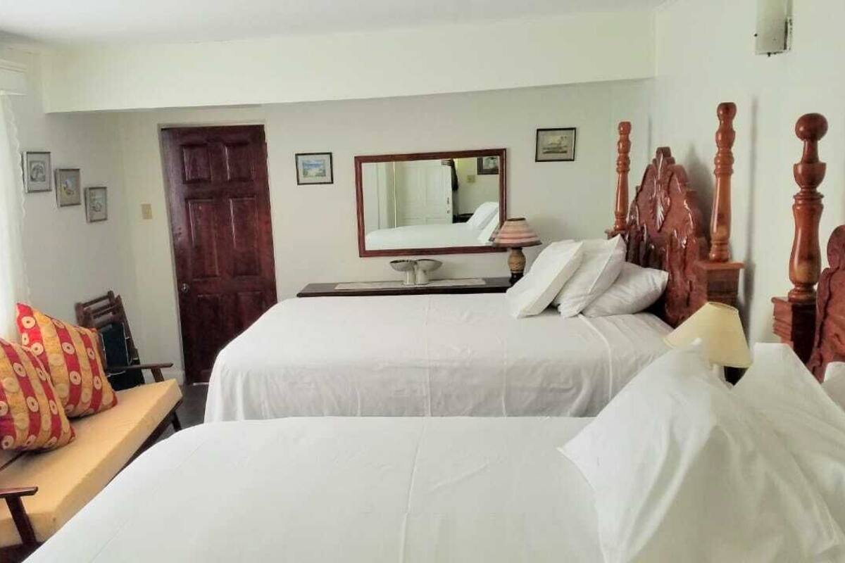 A hotel room with two beds, a wooden headboard, a desk with a lamp, and a large mirror.