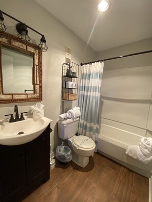 Une salle de bain avec un lavabo blanc, des toilettes, un miroir avec un cadre en bois, un rideau de douche et un porte-serviettes.