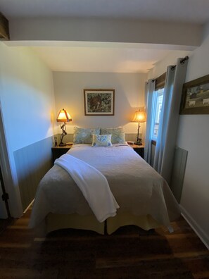 Une chambre à coucher avec un lit, deux lampes de chevet, un tableau encadré au mur et une fenêtre avec des rideaux.