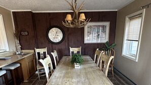 Comedor con mesa de madera, sillas, candelabro, reloj y ventana con persianas.
