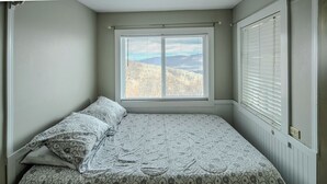 A bedroom with a bed, a window with blinds, and a view of a mountainous landscape. - Sugar Ski Economy Efficiency (no loft) - Unit 11-601 (Sugar Mountain)