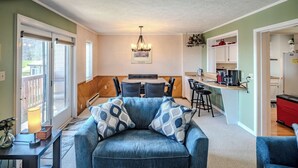 A living room with a blue sofa, dining table, and chairs, a kitchen area with a refrigerator and bar stools, and a hallway leading to another room. - Sugar Ski Comfort Two Bedroom - Unit 313 (Sugar Mountain)