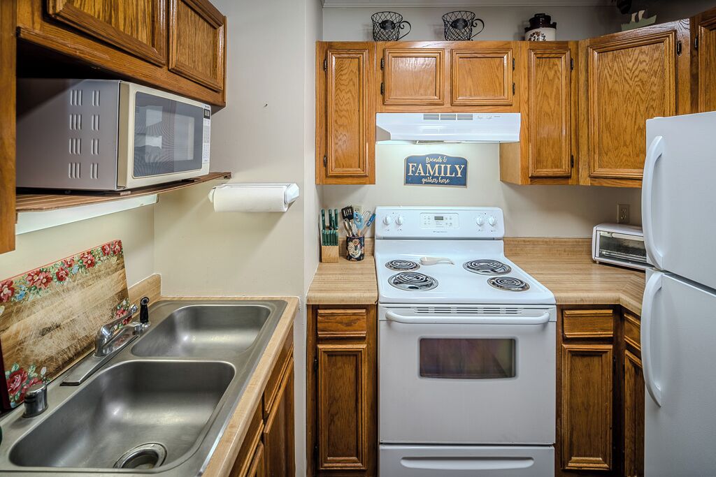 A compact kitchen with wooden cabinets, a white stove, a microwave, and a toaster.