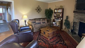 Een woonkamer met lederen fauteuils, een bank, een houten salontafel, een boekenkast, een open haard en een kamerbreed tapijt met dessin.