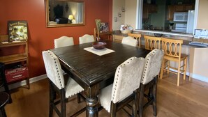 Een eethoek met een donker houten tafel, witte stoelen met kussens en een plafondventilator.