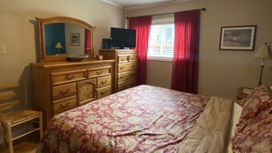 Een slaapkamer met een bed, een dressoir, een spiegel, een televisie en een plafondventilator.