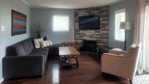 Una sala de estar con chimenea de piedra, un televisor de pantalla plana, un sofá, una mesa de centro y una lámpara.