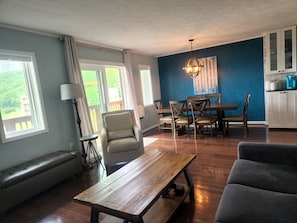 A dining area with a wooden table and chairs, a bench, and a view of greenery outside.
