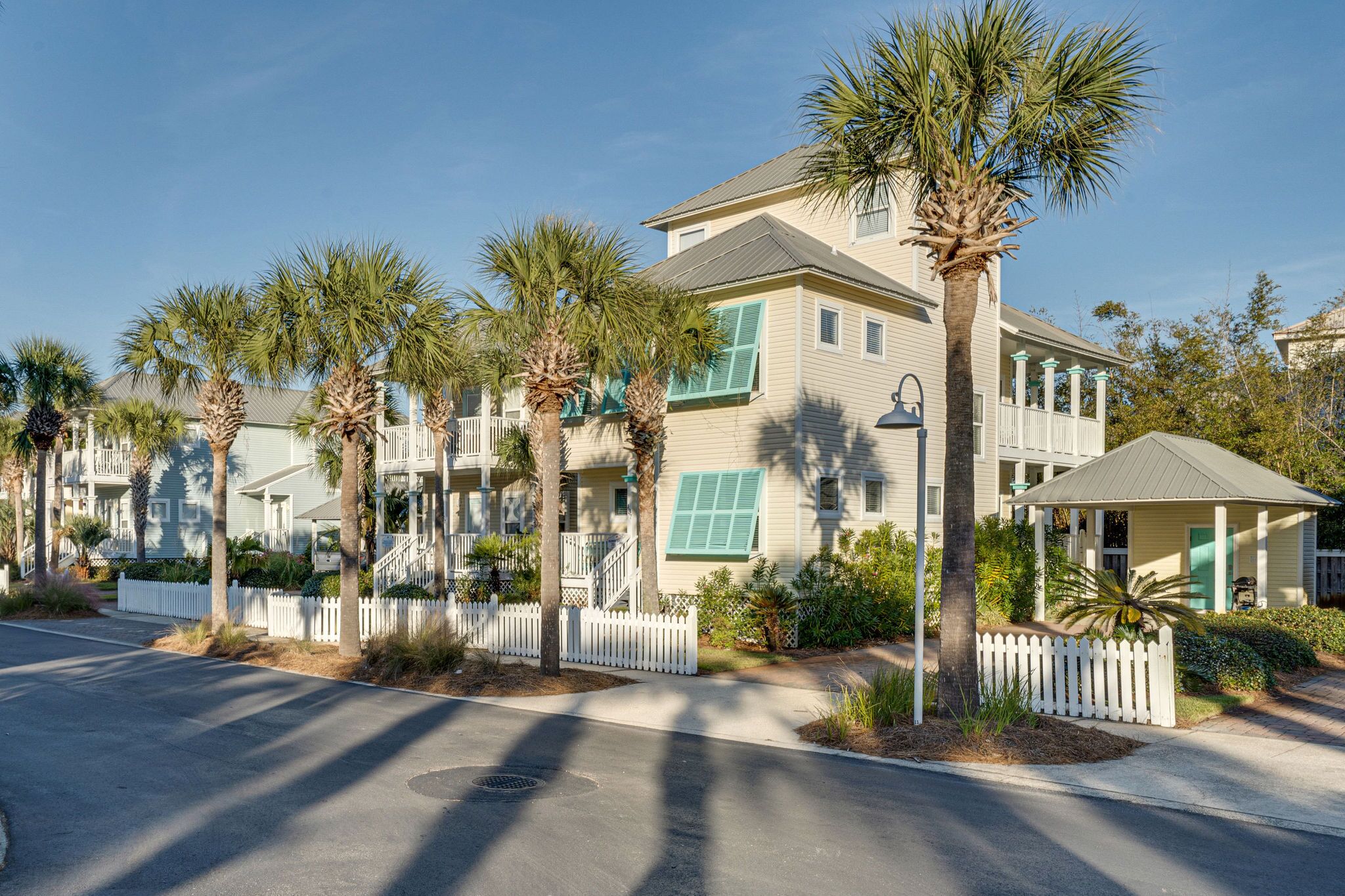 A row of two-story buildings with a white picket fence, palm trees, and a clear blue sky.