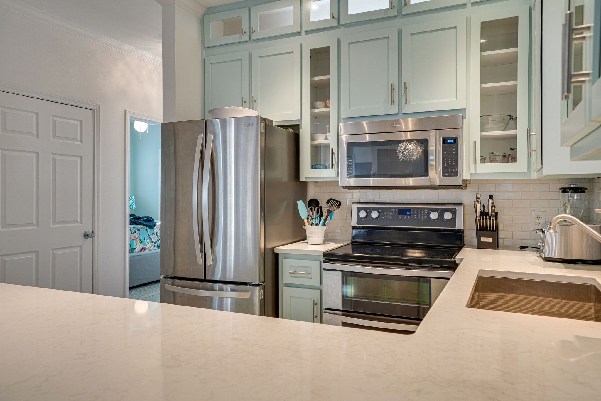 A modern kitchen with stainless steel appliances, light blue cabinets, and a white countertop.
