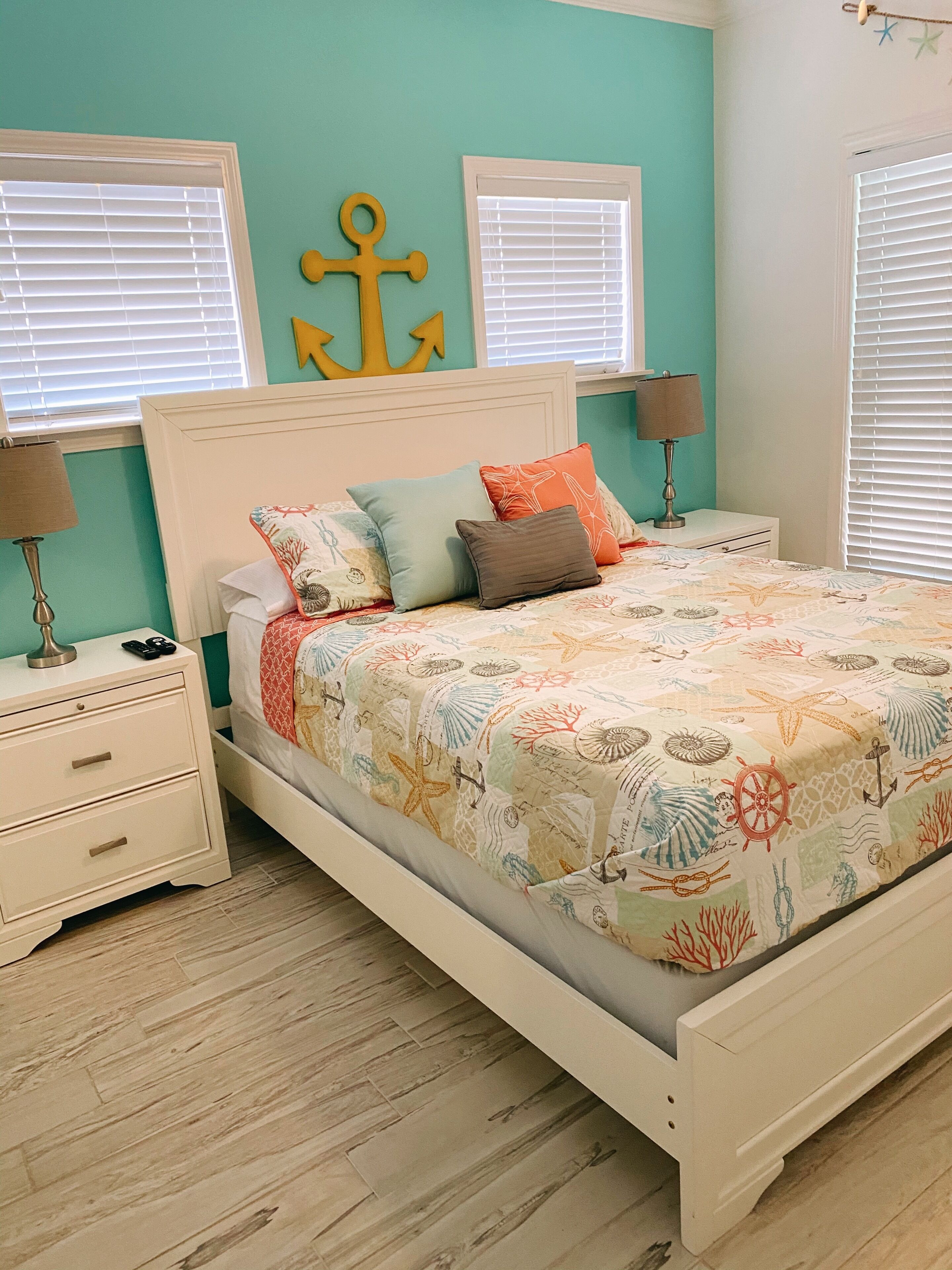 A bed with a nautical-themed bedspread, two bedside lamps, and a nightstand with drawers.