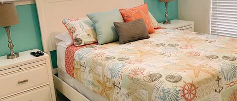 A bed with a nautical-themed bedspread, two bedside lamps, and a nightstand with drawers.
