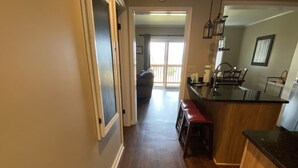 Un pasillo con suelo de madera que conduce a una zona de cocina con barra y un comedor con mesa y sillas.
