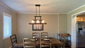 Un comedor con mesa y sillas de madera, una araña y un refrigerador al fondo.