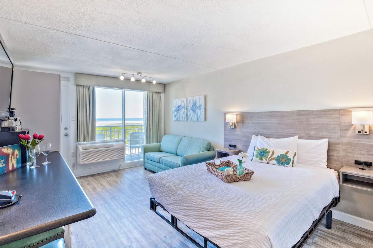 Een hotelkamer met een bed, een bureau met een computer, een stoel, een raam met uitzicht en een balkon.